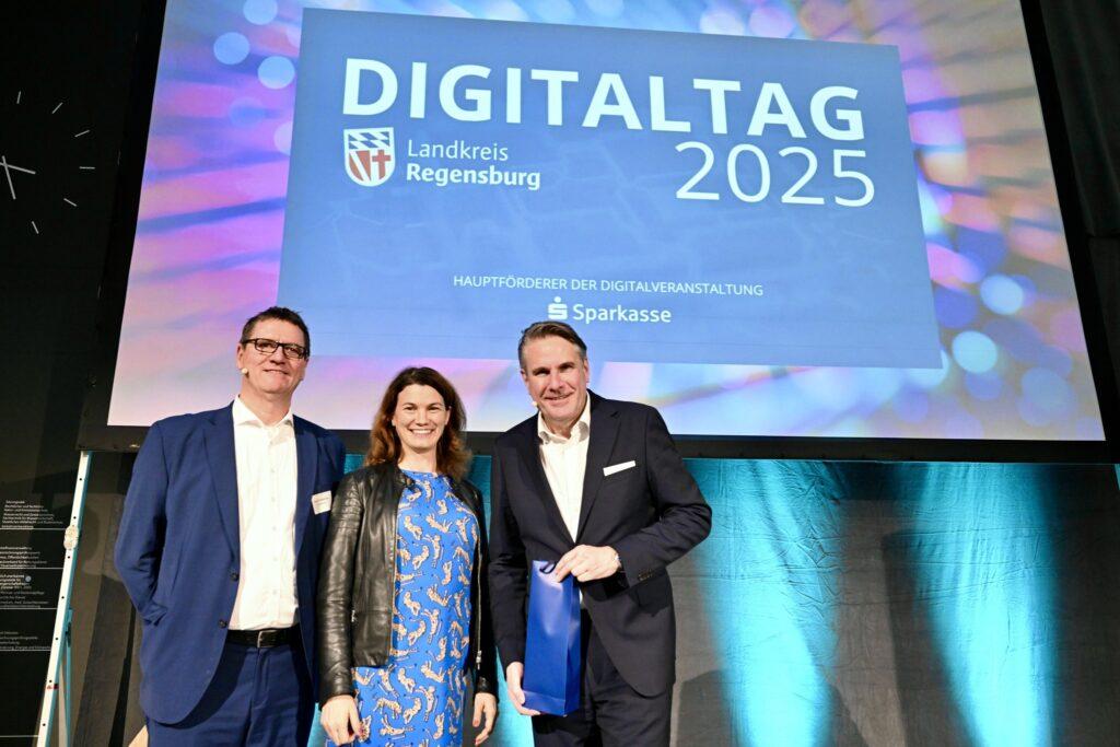 Abteilungsleiter Öffentlichkeitsarbeit und Digitalisierung Landratsamt Regensburg Harald Hillebrand, Landrätin Tanja Schweiger und Keynote-Speaker Dr. Christian Stummeyer auf der Bühne der Veranstaltung „Vorne mit dabei – Digitalisierung im Landkreis Regensburg“